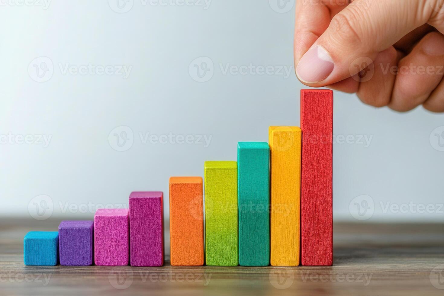 Colorful wooden blocks arranged in a growth chart, with a hand adding to the highest bar photo