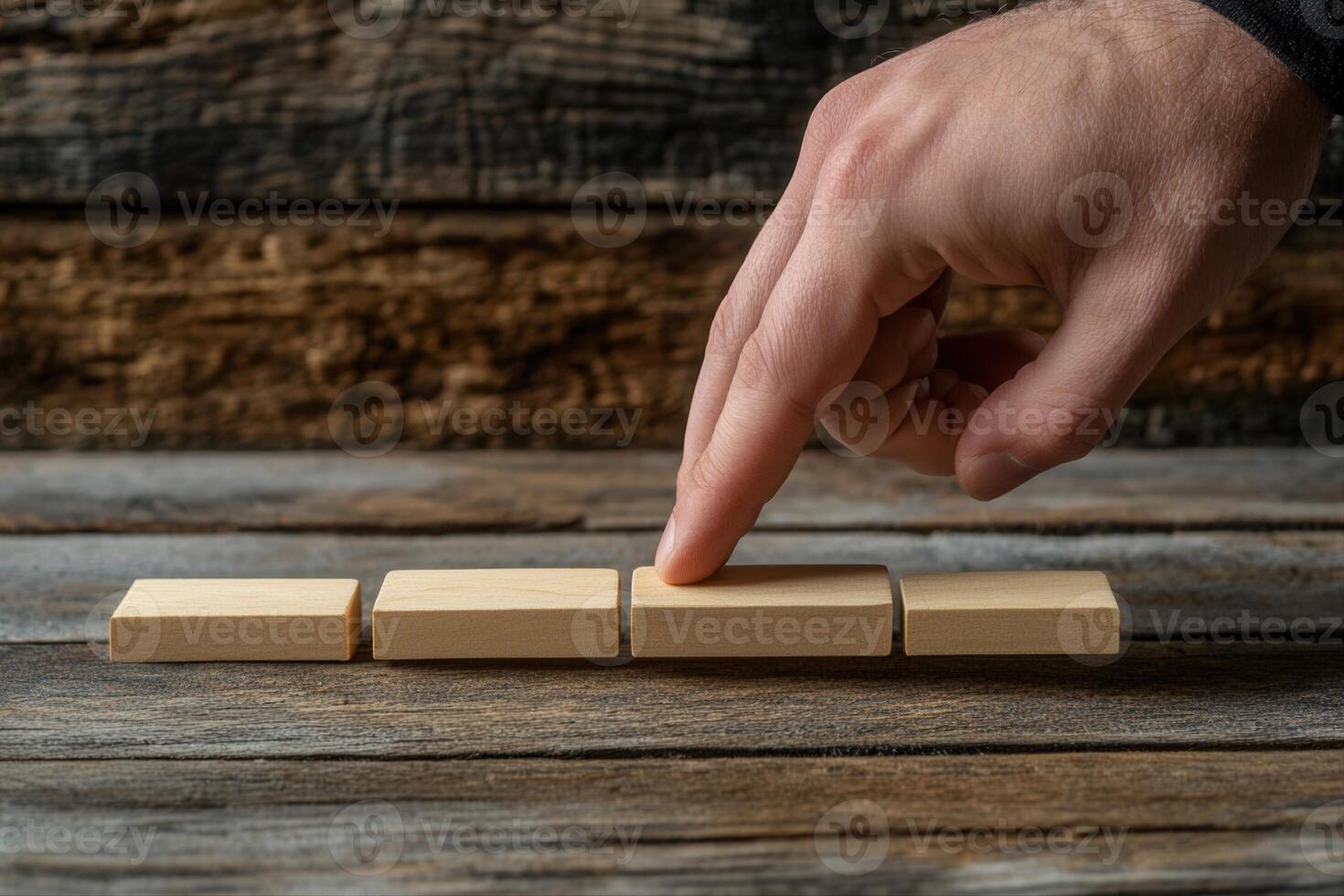 A hand gently pressing down on wooden blocks arranged in a row on a rustic table photo