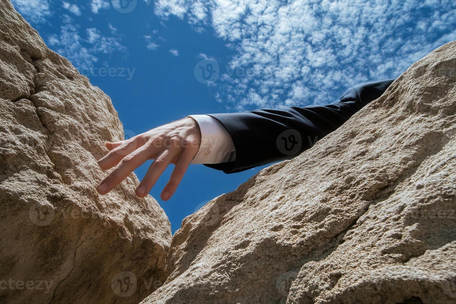 A businessman in a suit reaches out from between two rocky cliffs under a blue sky photo