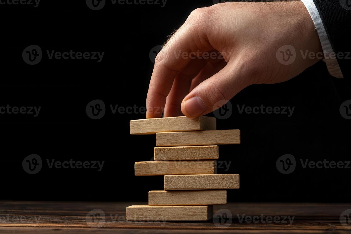 Hand carefully placing a wooden block on a tower of blocks against a dark background photo
