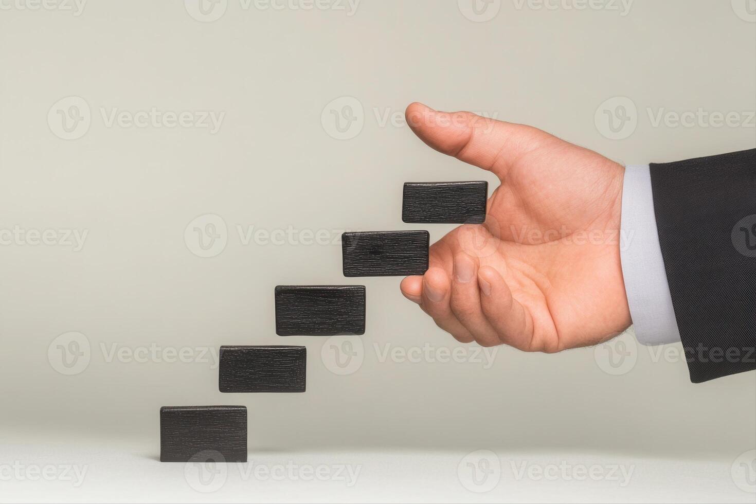 Hand in a suit placing black blocks in a staggered arrangement on a flat surface photo