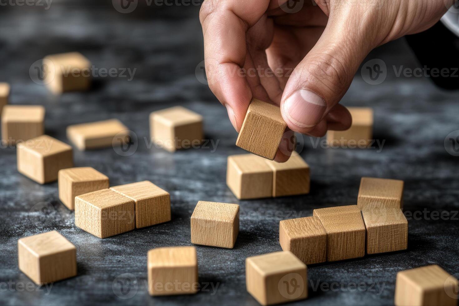 Hand arranging wooden blocks on a textured surface with scattered blocks in the background photo