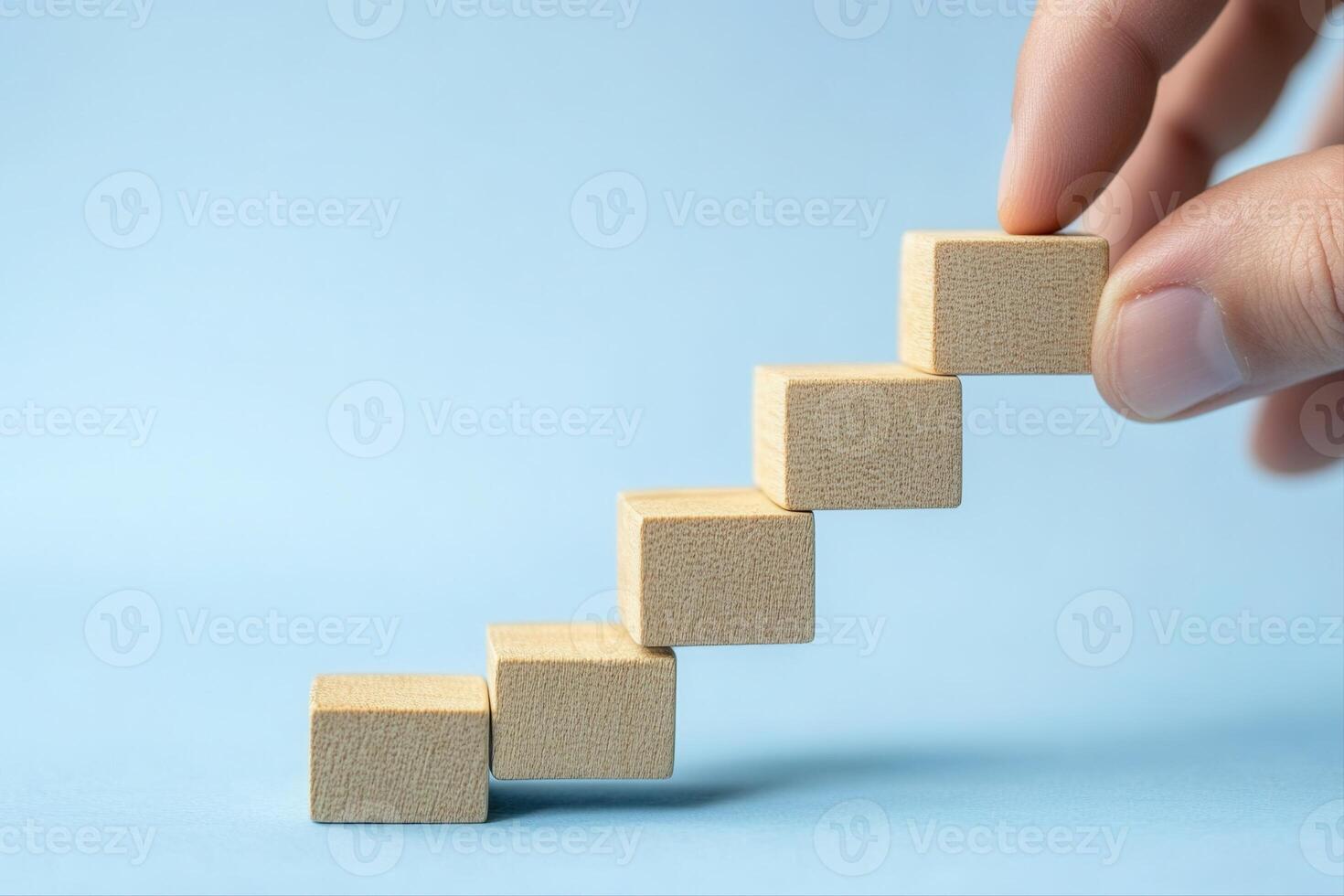 Hand placing wooden blocks in a step formation on a blue background, symbolizing growth photo