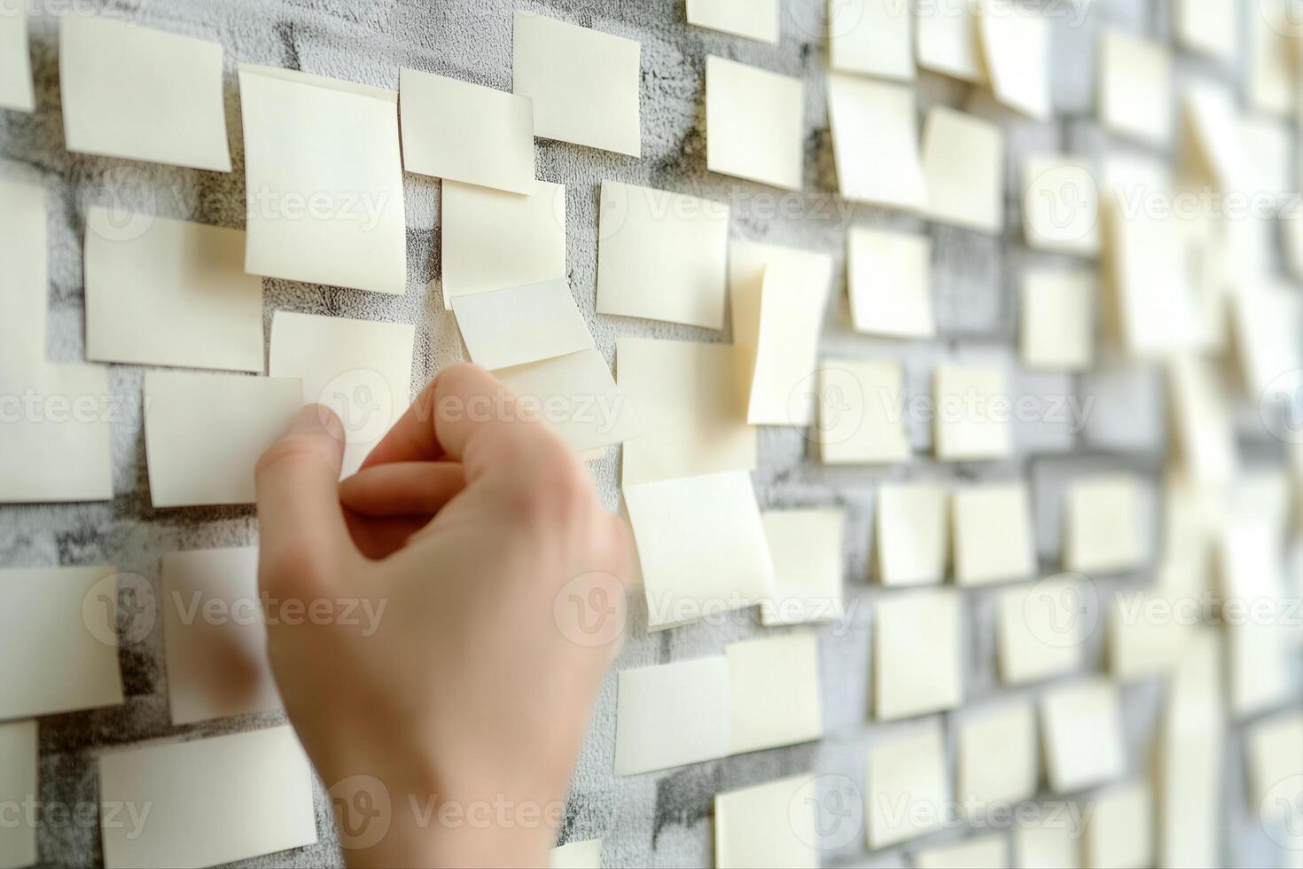 Hand placing a sticky note on a textured wall filled with blank notes, symbolizing ideas photo