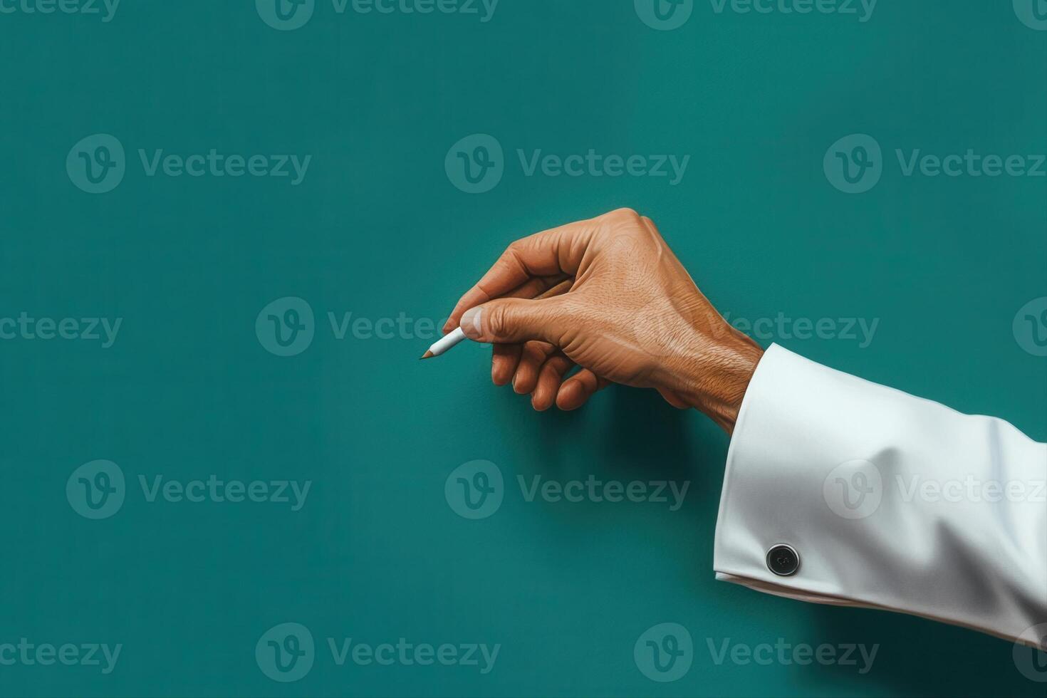 Hand holding a pen poised to write on a green chalkboard in a classroom setting photo