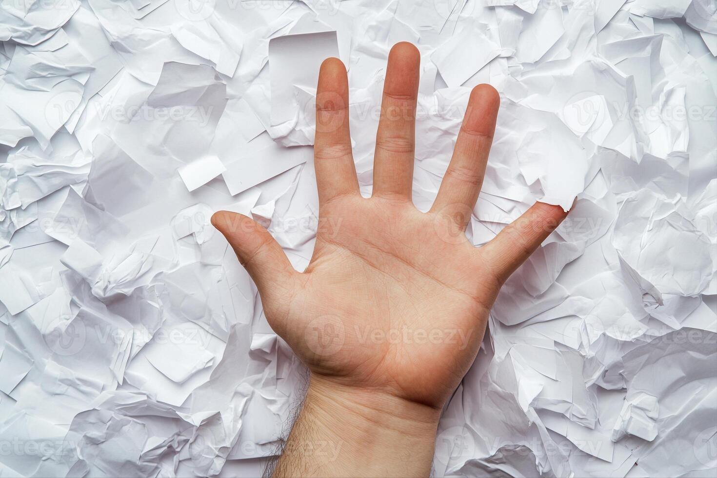 Hand reaching out amidst crumpled paper, symbolizing struggle or frustration in work photo