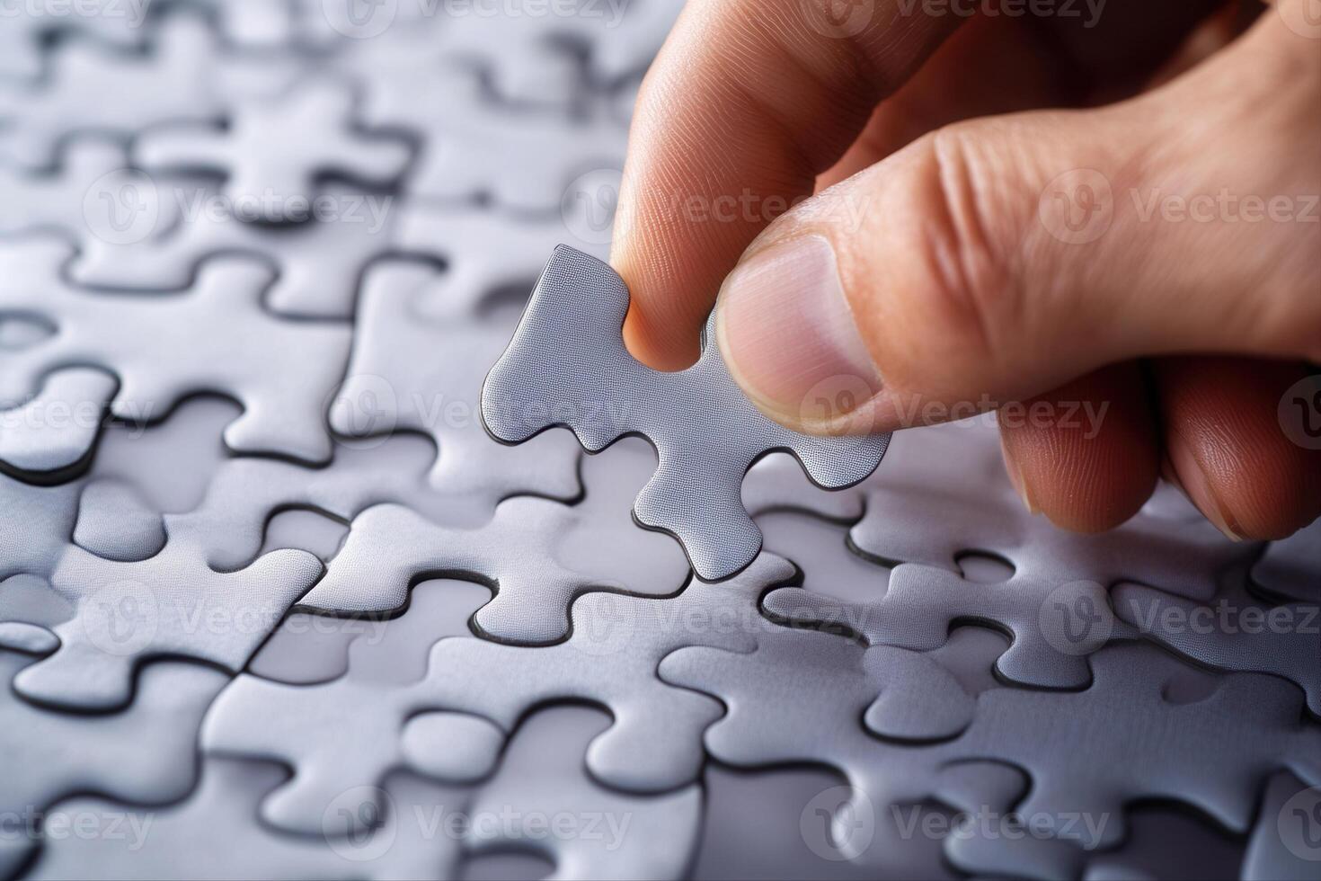 Hand placing a puzzle piece onto a nearly completed gray puzzle on a table photo
