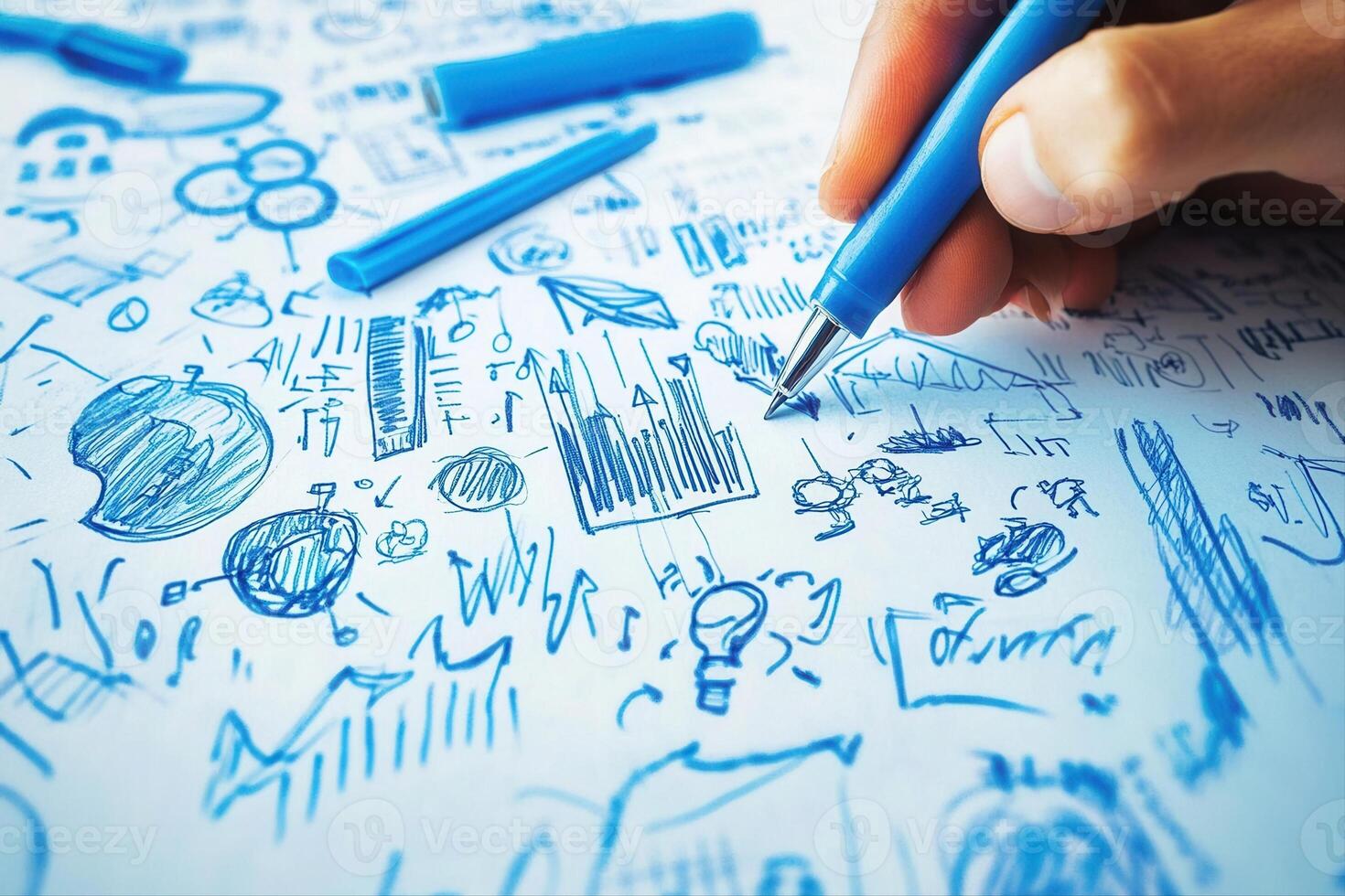 Hand holding a blue pen, sketching creative ideas on paper filled with doodles and diagrams photo