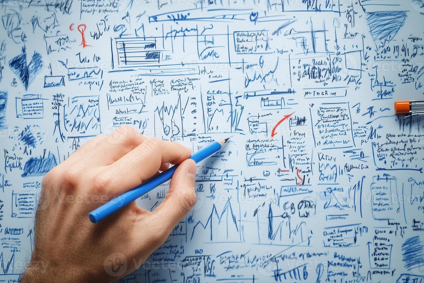 Hand holding blue pencil writing on chaotic paper filled with graphs and notes photo