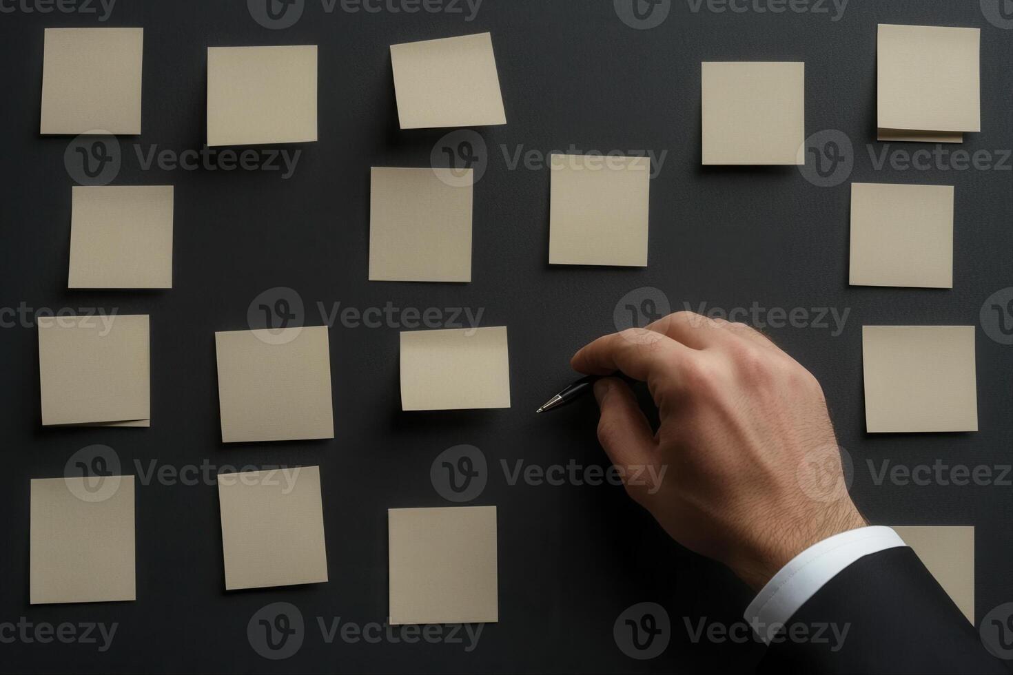 Hand placing a pen on blank sticky notes arranged on a dark surface, ideal for brainstorming photo