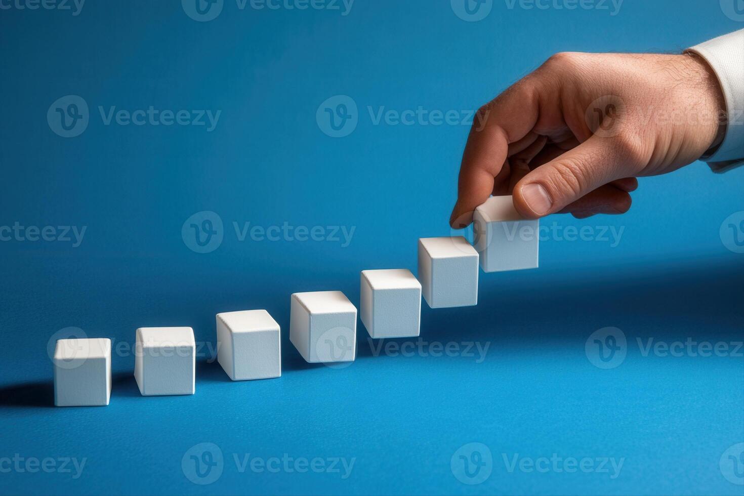 Hand placing a white cube on a growing stack of cubes against a blue background photo