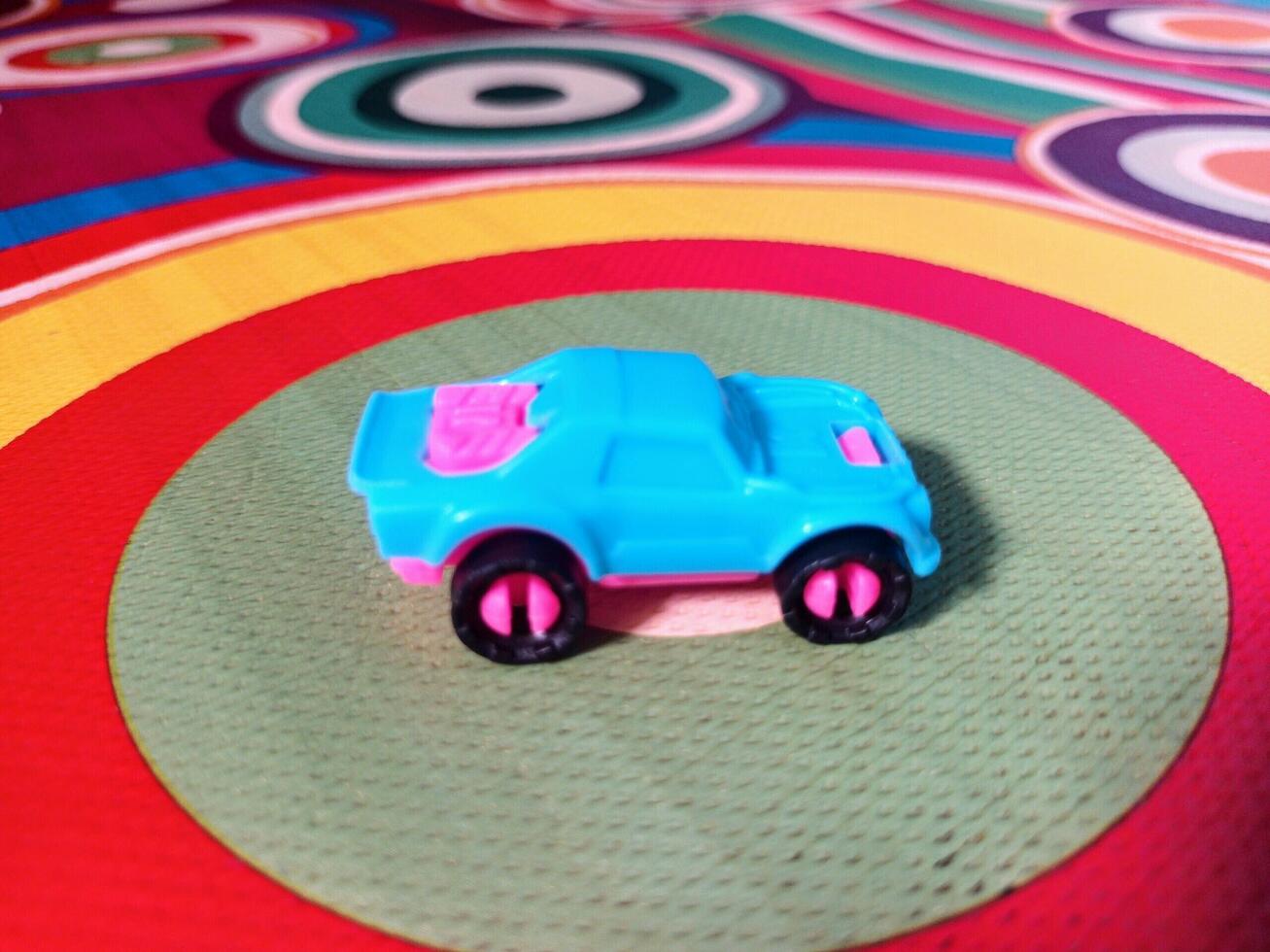 A Small Light Blue and Pink Toy Car on a Multicolored Circular Patterned Mat. photo