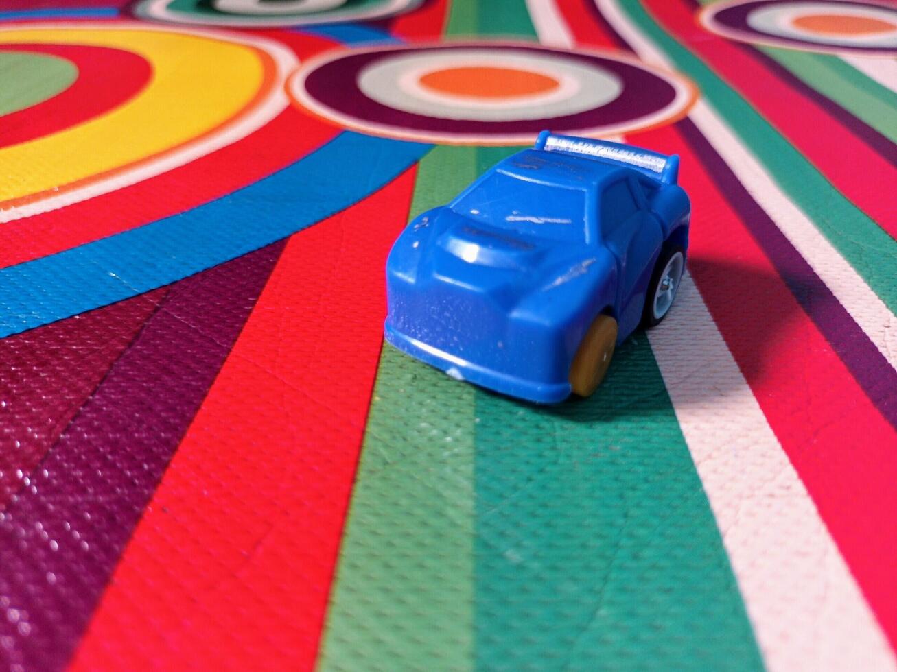 A Small Blue Toy Car on a Multicolored Circular and Striped Patterned Surface. photo