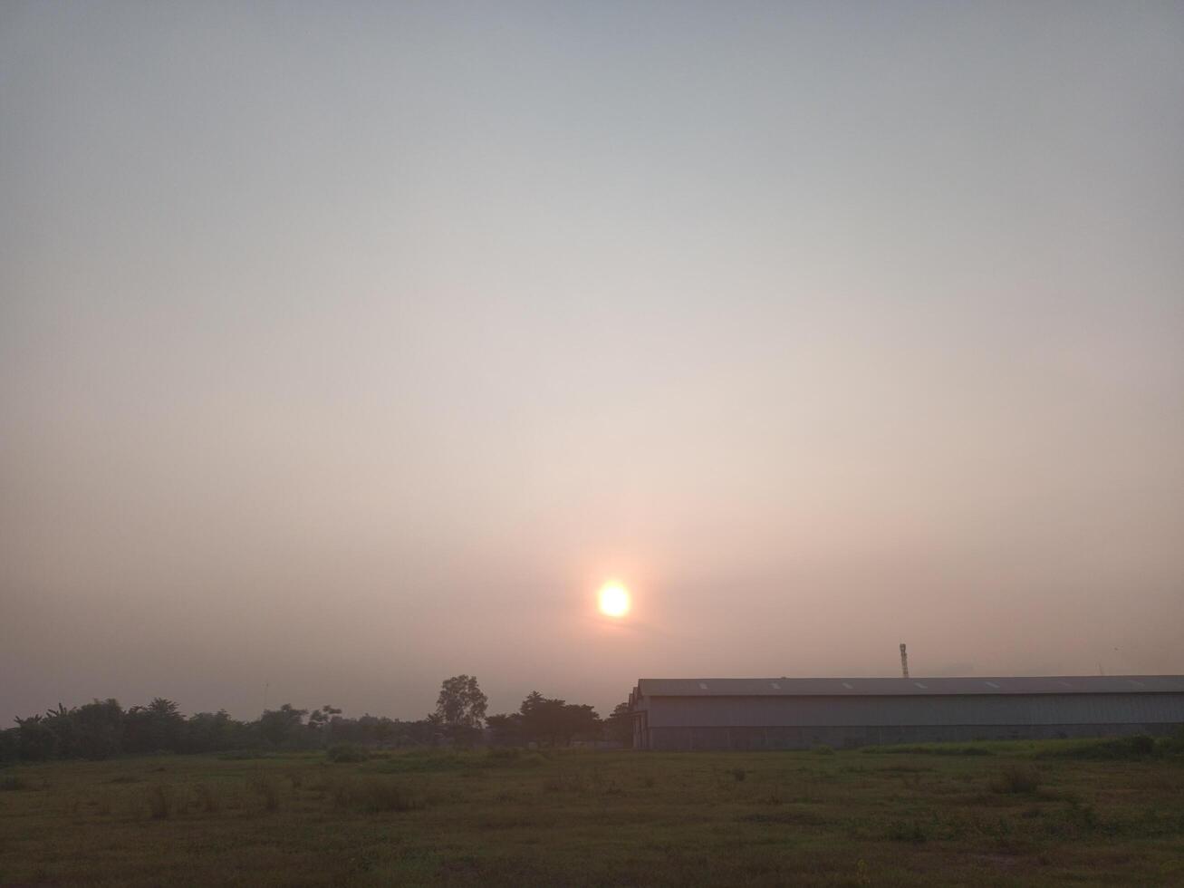 A field with a barn and a sun setting behind it photo