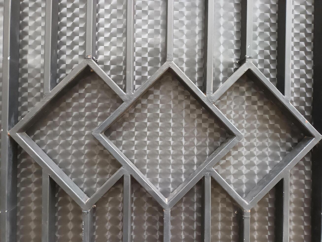 Close-up of a Black Metal Gate with Diamond-Shaped Openings Against a Patterned Background. photo