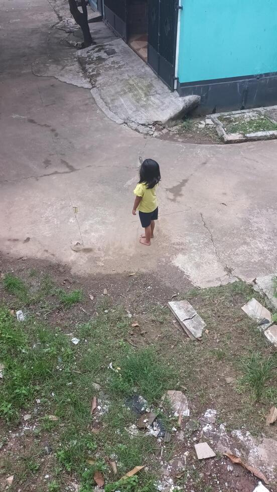 A Young Child in a Yellow Shirt Standing Barefoot on a Concrete Surface. photo