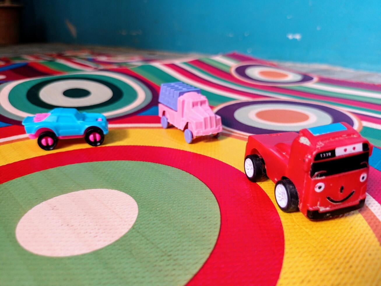 Three Small Toy Vehicles on a Multicolored Circular Patterned Mat. photo