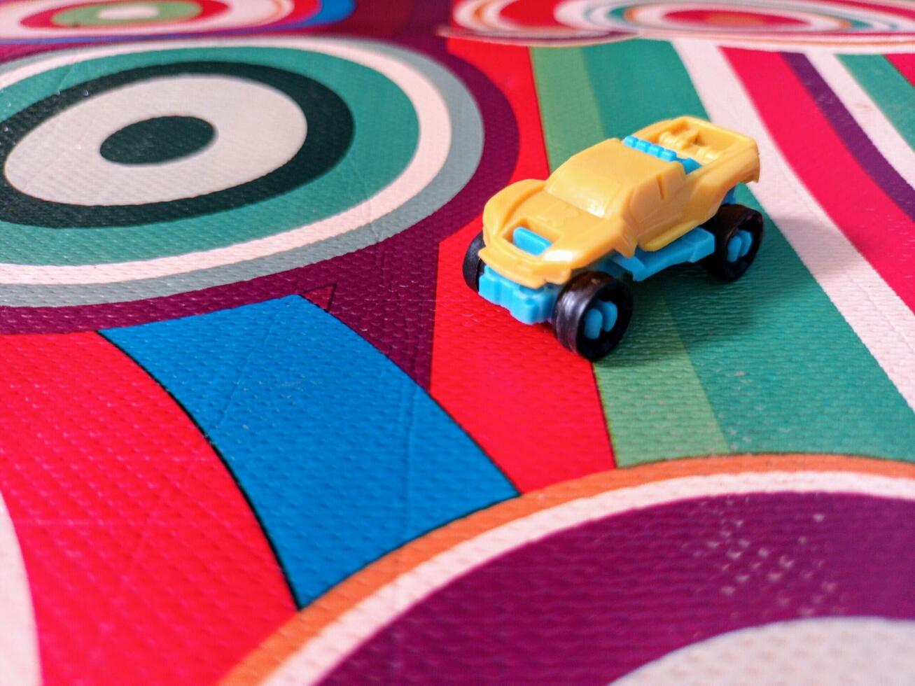 A Small Yellow and Blue Toy Truck on a Colorful Circular Patterned Surface. photo