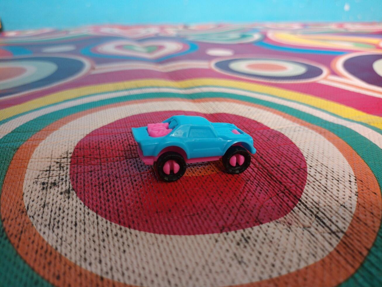 A Small Light Blue and Pink Toy Car on a Colorful Circular Patterned Textile. photo