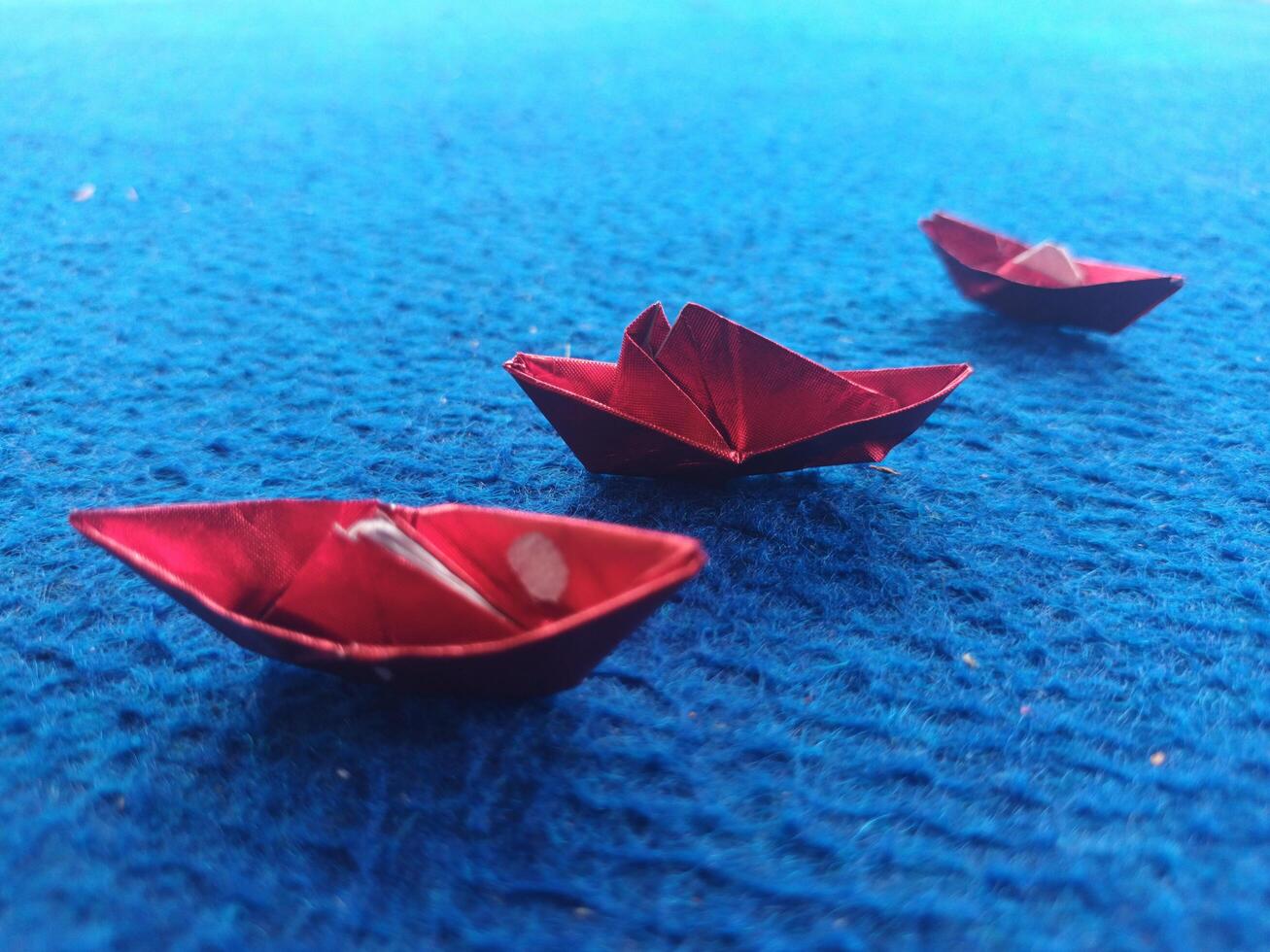 Three Small Red Origami Boats on a Textured Blue Surface. photo