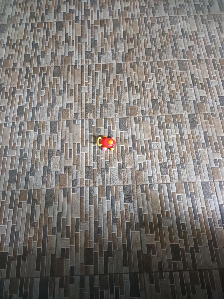 Small Red and Yellow Toy on Rectangular Patterned Floor Tiles. photo