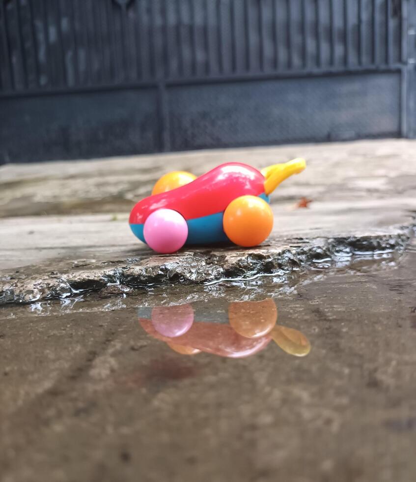 A Colorful Toy Car Reflected in a Puddle on a Concrete Surface. photo