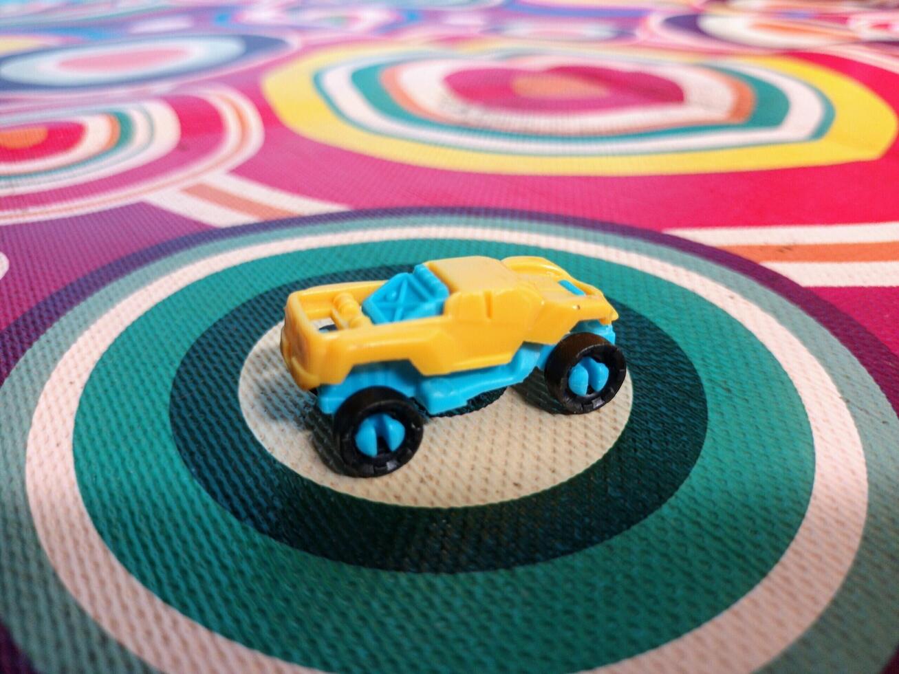 A Small Yellow and Blue Toy Truck on a Multicolored Circular Patterned Fabric. photo