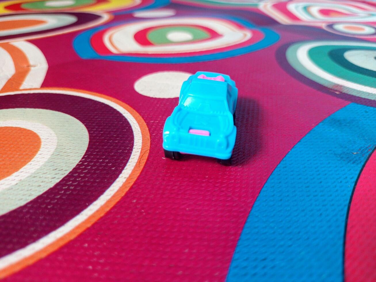 A Tiny Blue and Pink Toy Car on a Multicolored Circular Patterned Mat. photo