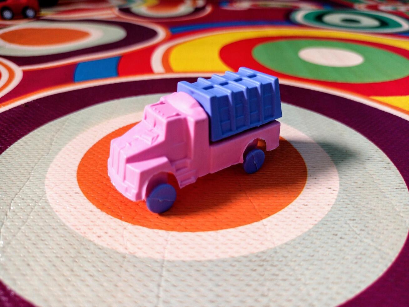 A Small Pink and Blue Toy Truck on a Colorful Circular Patterned Mat. photo