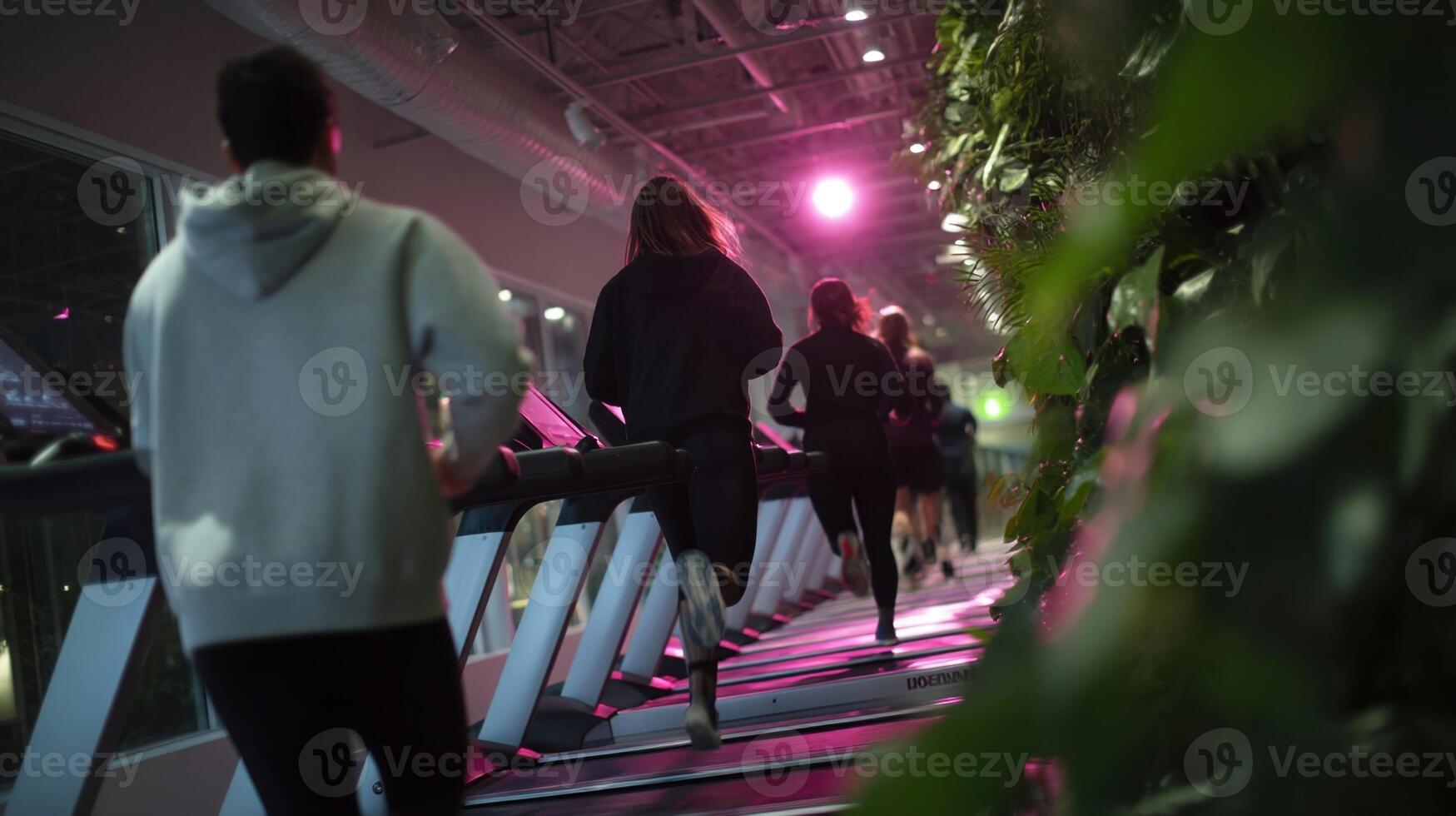 A cluster of friends cheer each other on laughter punctuating their tireless effort. One climber arms extended pushes upward grasping a remote control. The treadmills settings ram photo