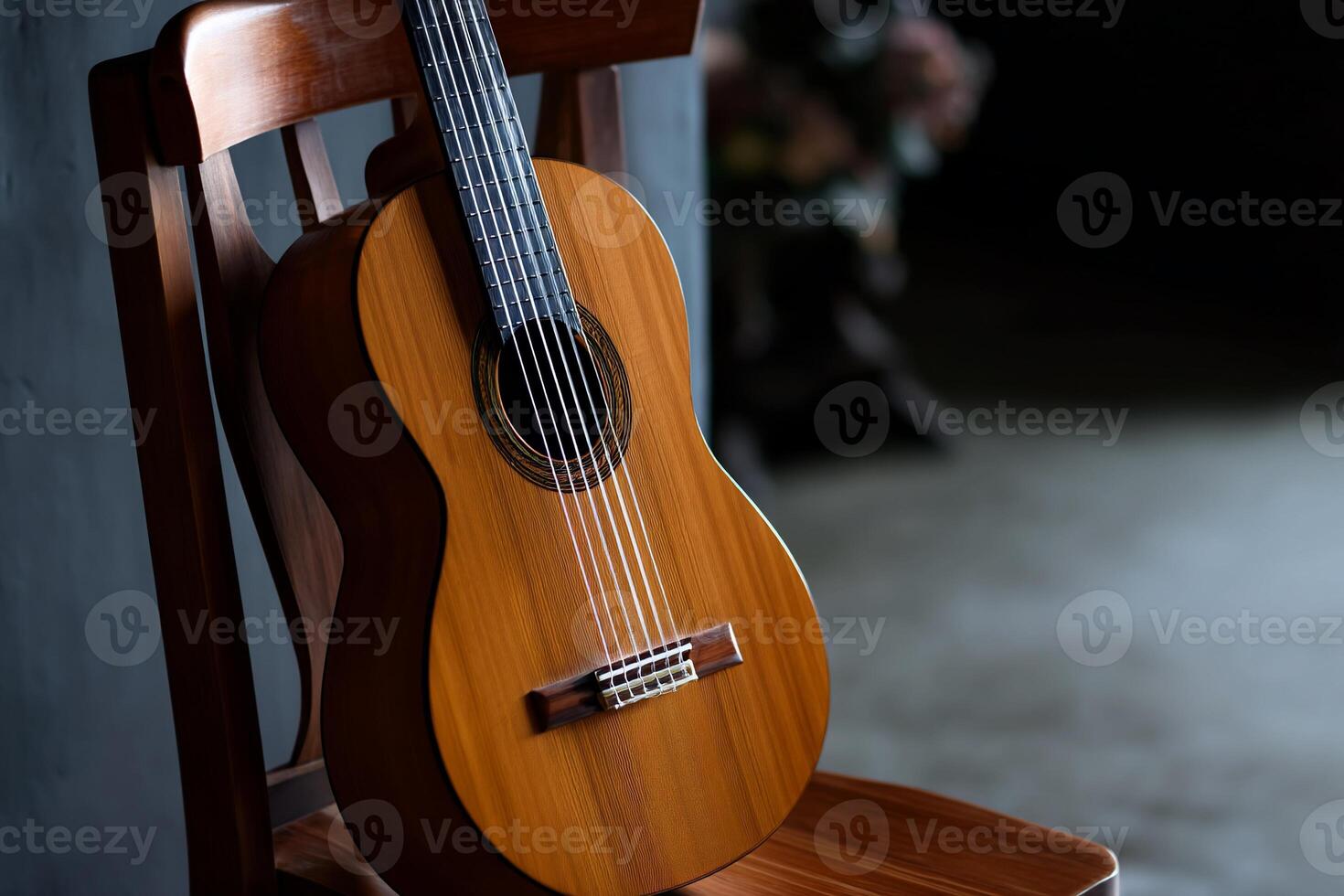 Classical guitar resting on wooden chair. Wooden guitar body, strings, and fretboard are visible. Dark background photo