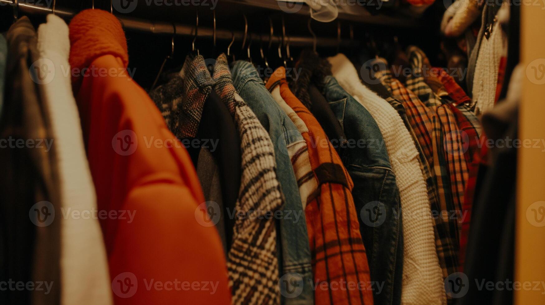 Close-up of clothes hanging in a closet. Various colors and patterns on jackets, shirts, and blouses photo
