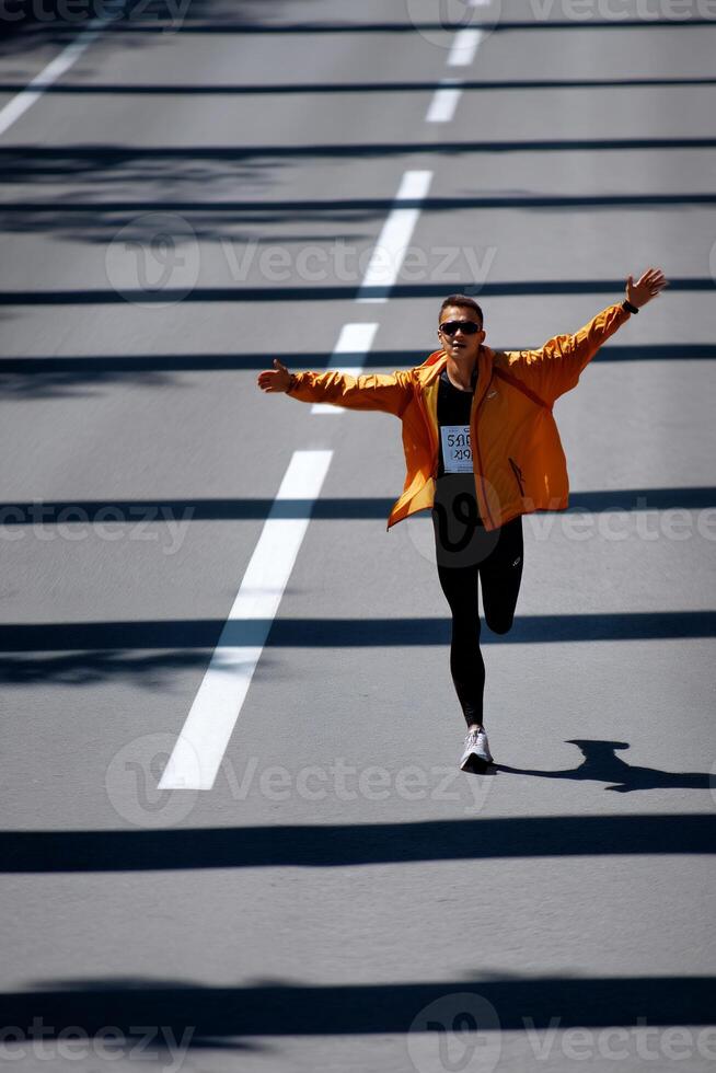 Runner celebrates a successful race on asphalt road. Long shadows and white stripes on the pavement photo