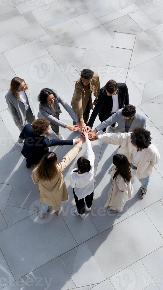 Diverse group joining hands in a circle on light-colored pavement. Teamwork, unity, collaboration, and support are evident photo