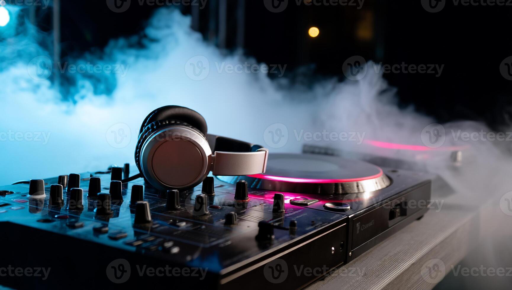 DJ equipment on a table, illuminated by colored lights, with headphones and turntables, amidst smoky atmosphere photo