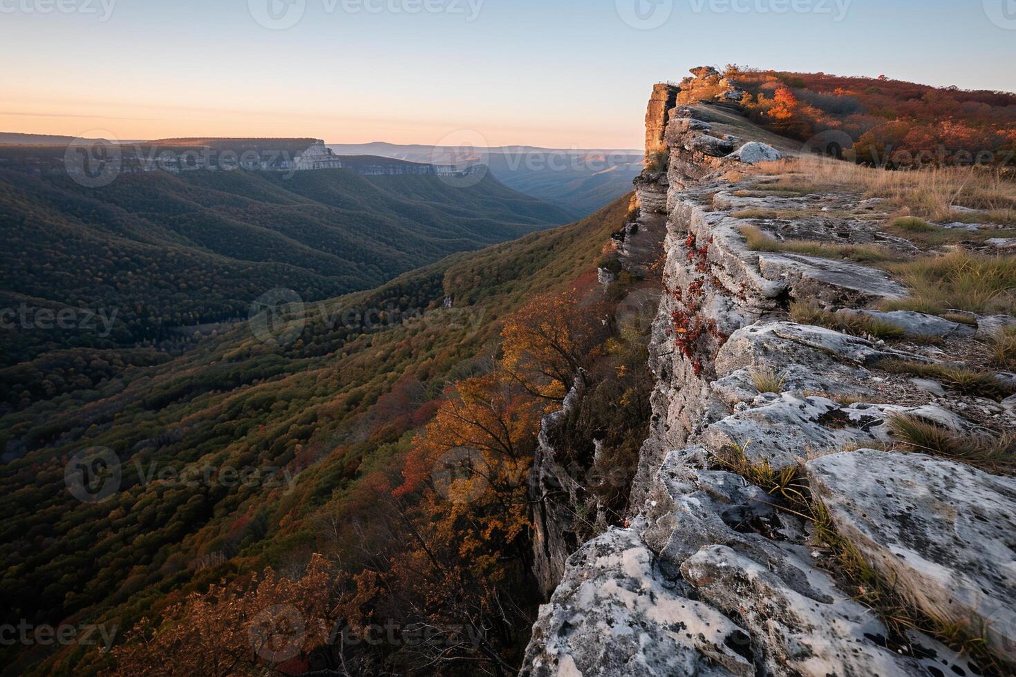 Mountain peak edge at autumn sunrise. Vast valley, colorful foliage, and light stone photo
