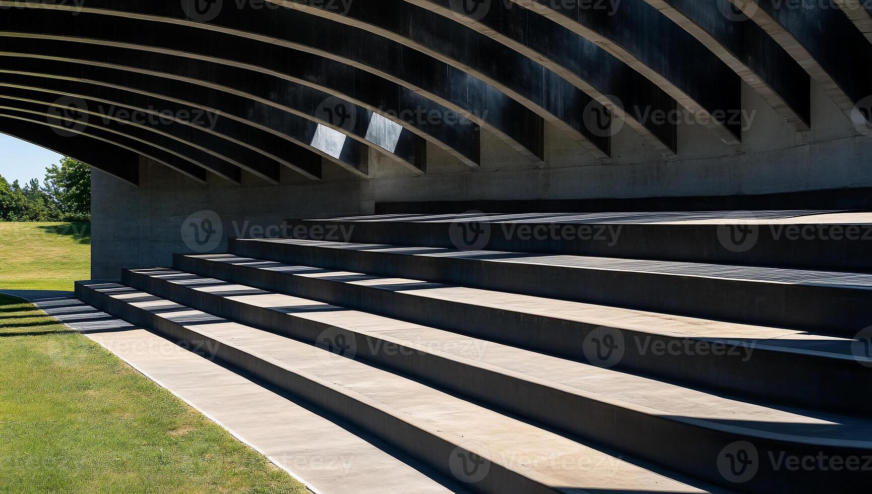 Modern concrete bleachers under a curved metal roof, overlooking a grassy field photo
