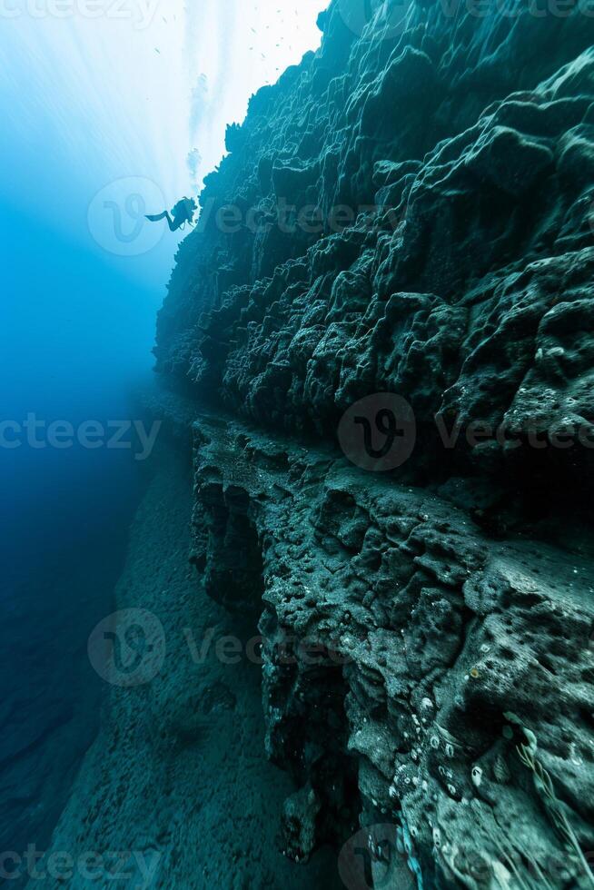 Underwater dive site, dark rocky cliff face, deep blue ocean. Diver silhouette photo