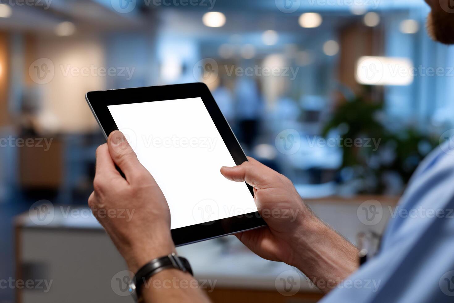 Close-up of a person holding a tablet computer. Person's hands hold a blank tablet screen. Blurred office background photo