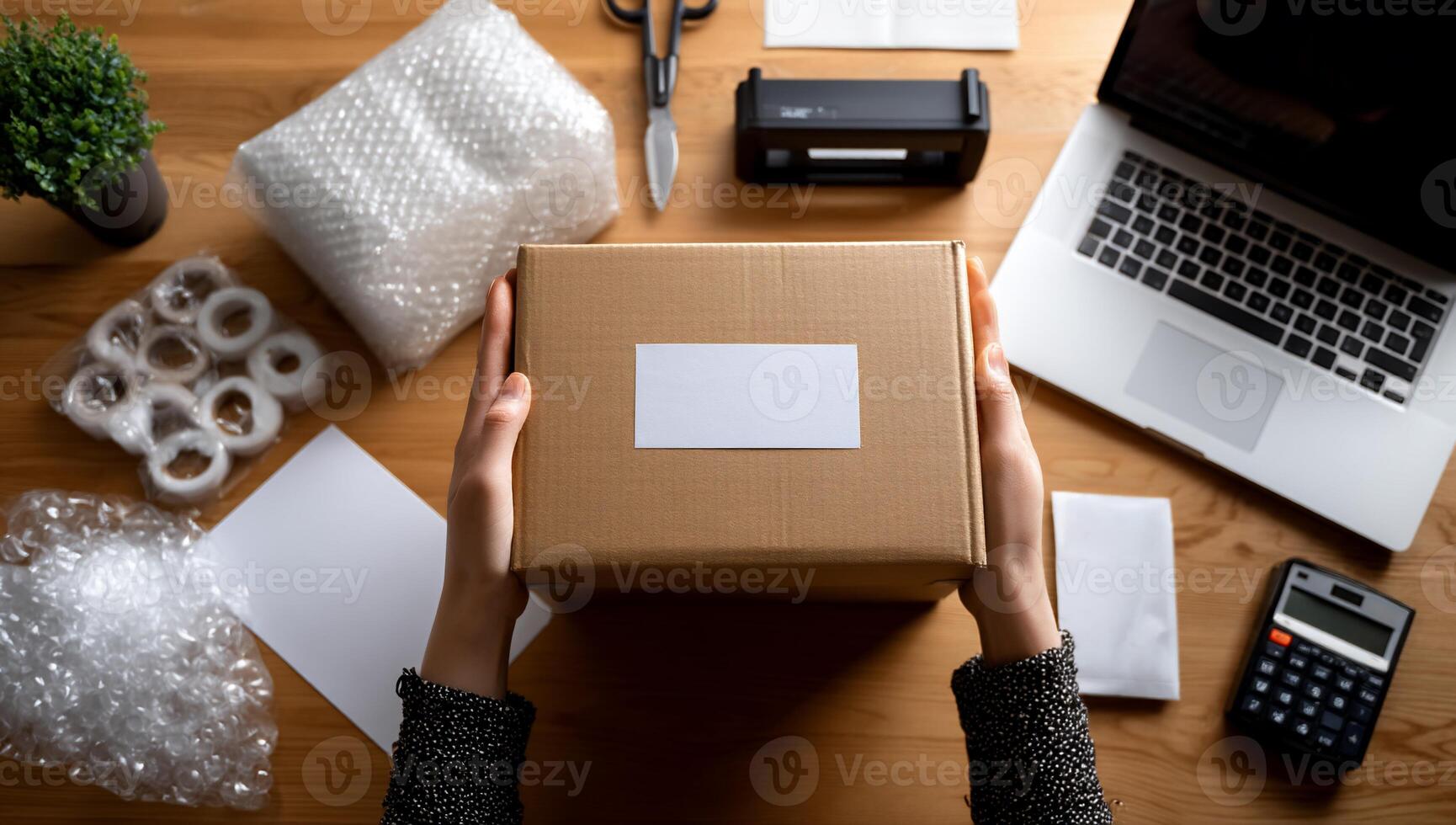 Hands holding a cardboard box with blank label, surrounded by packing supplies and office items photo