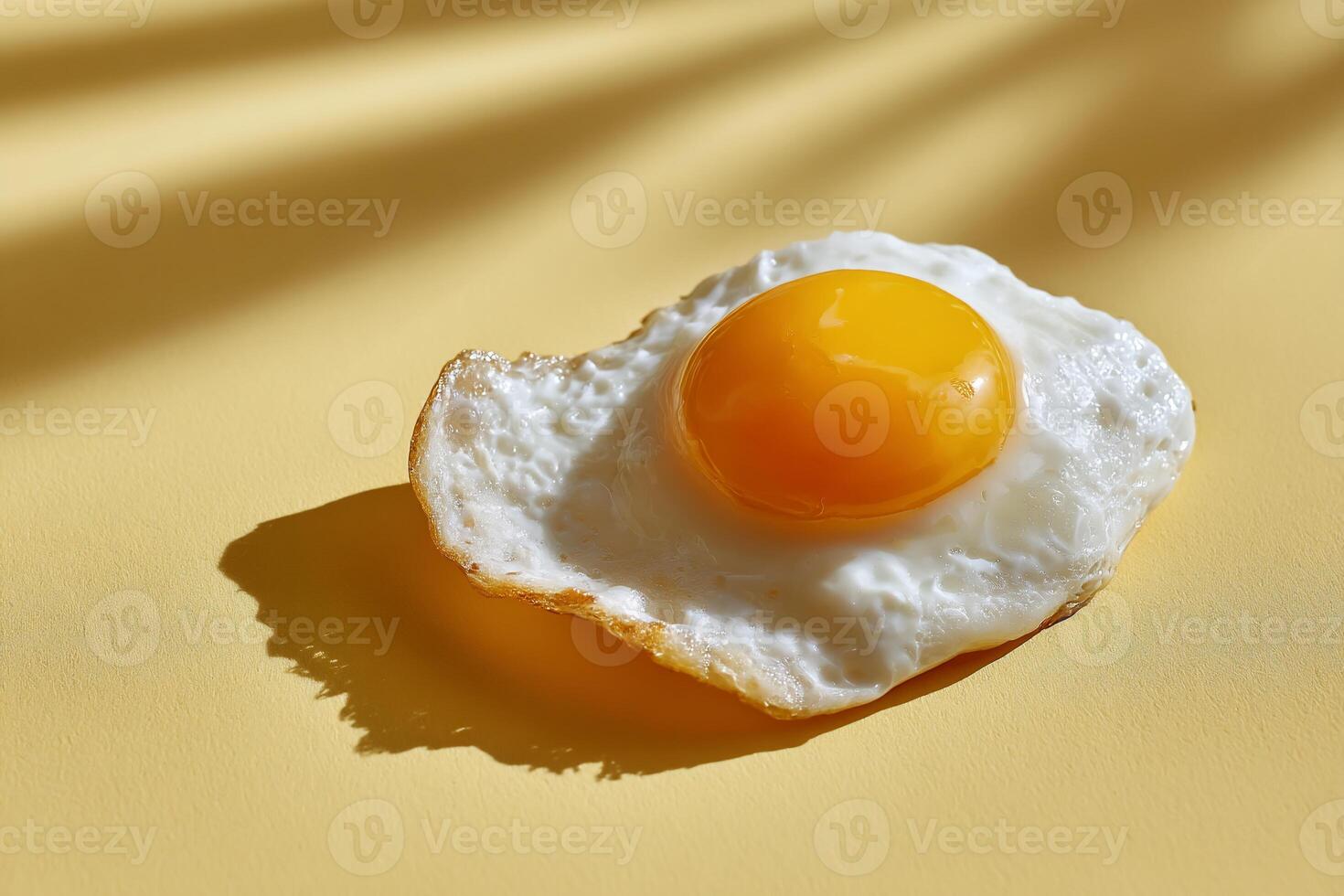 Single fried egg on a pale yellow surface, sunlight casts shadows. The egg is cooked, with a runny yolk photo