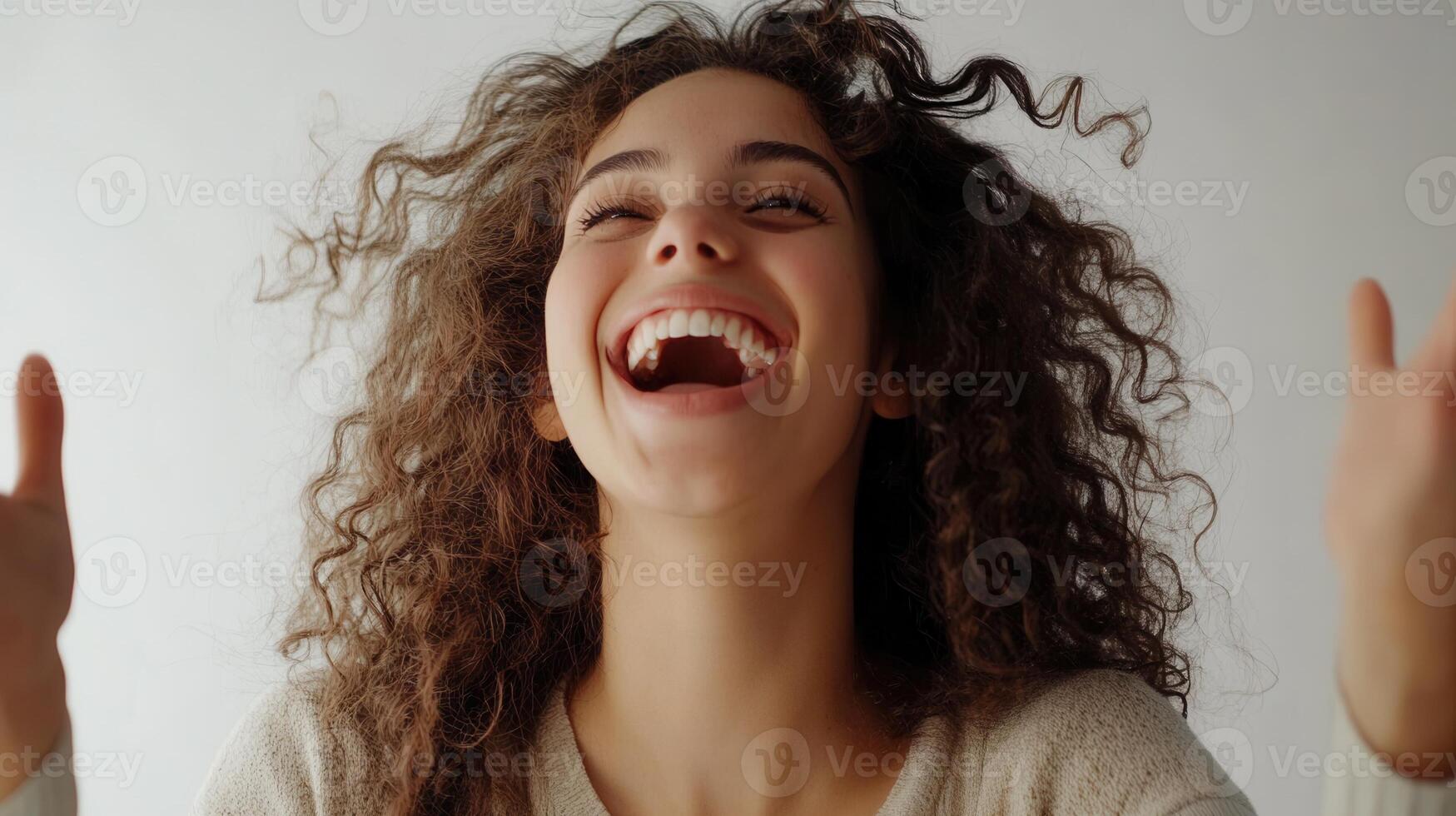 A joyful happiness young with emotion woman curly hair, grinning widely and raising her hands in excitement, framed by a white background photo