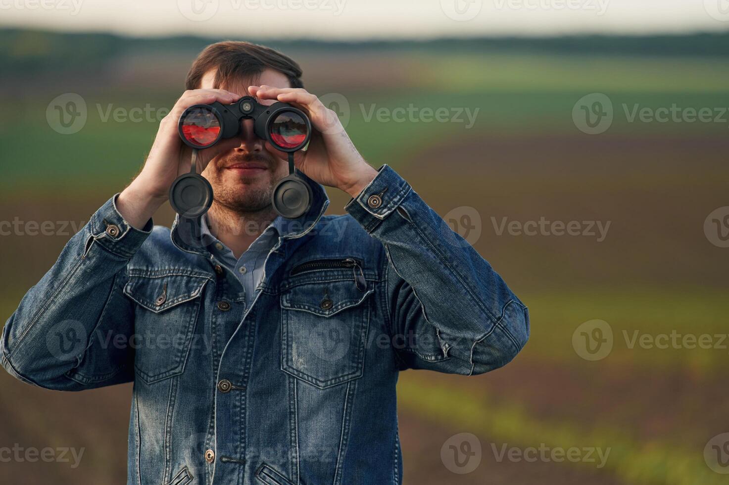 Portrait of man with binoculars that is standing outdoors on the agricultural field photo