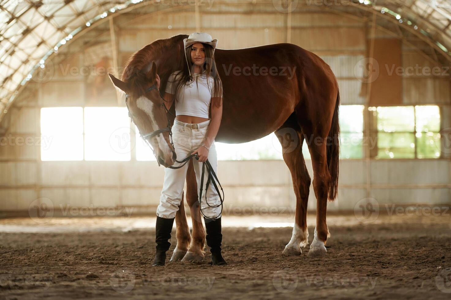 In the cowboy hat... Beautiful young woman is with horse indoors photo