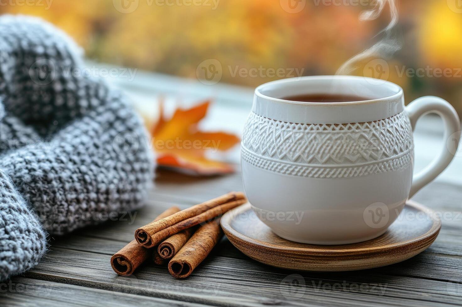 Warm beverage, cinnamon sticks, and cozy sweater create a comforting autumn scene by the window photo