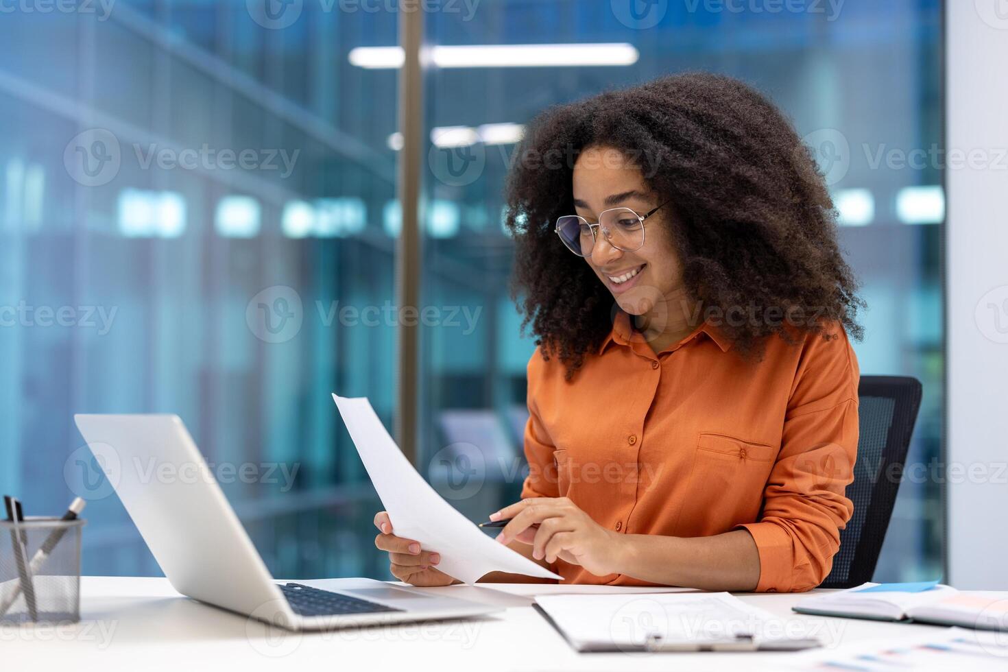 Successful businesswoman at workplace inside office working with documents, reports and contracts. Woman smiling happily, using laptop at work. photo
