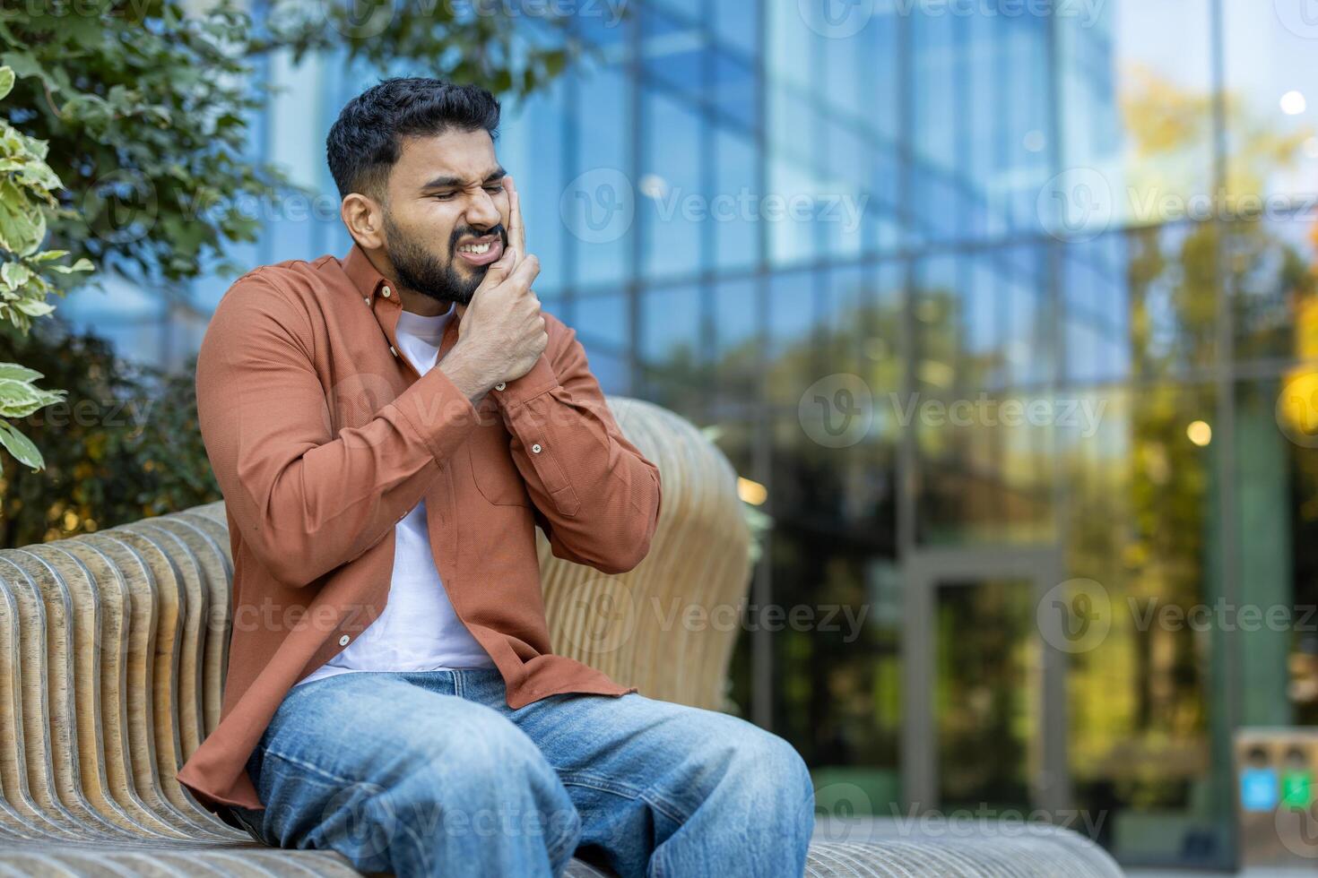 A man with a pained expression clutches his jaw, clearly suffering from a toothache while sitting on a bench. photo