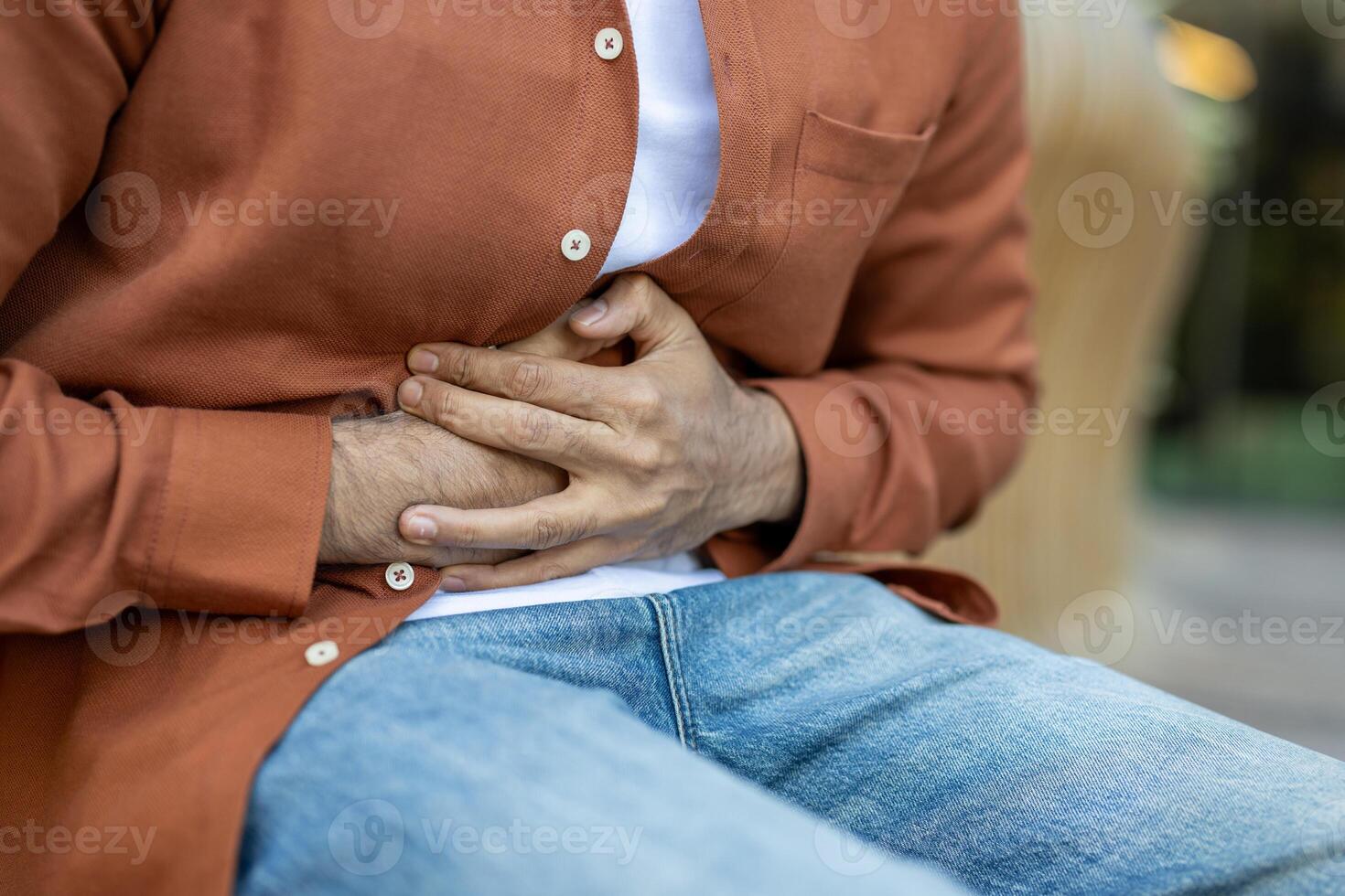 A man clutches his abdomen, suggesting abdominal discomfort or pain. The image highlights the pose, conveying a sense of physical distress or health concern. photo