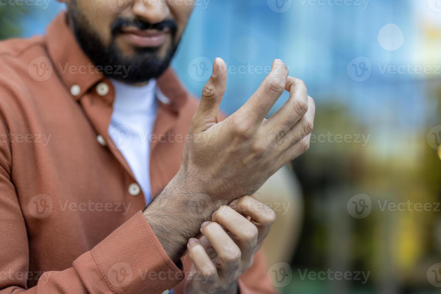 A man scratches his wrist, possibly due to itching or discomfort. The focus is on his hands and part of his face. photo
