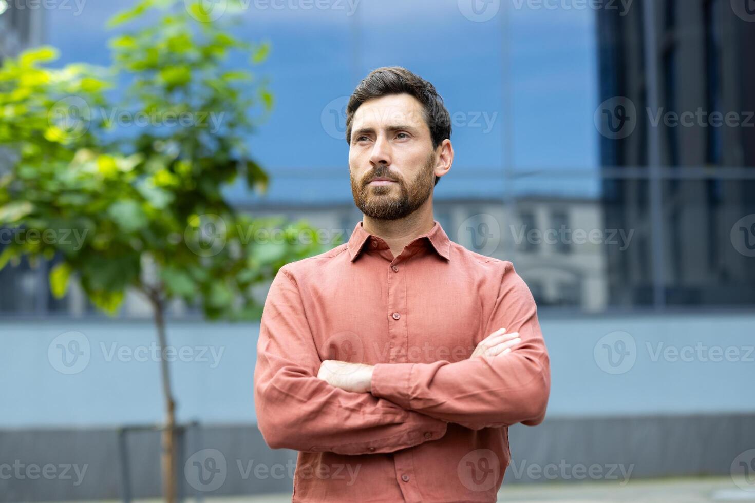 A handsome man stands confidently with folded arms in front of a modern building, exuding a sense of poise. photo